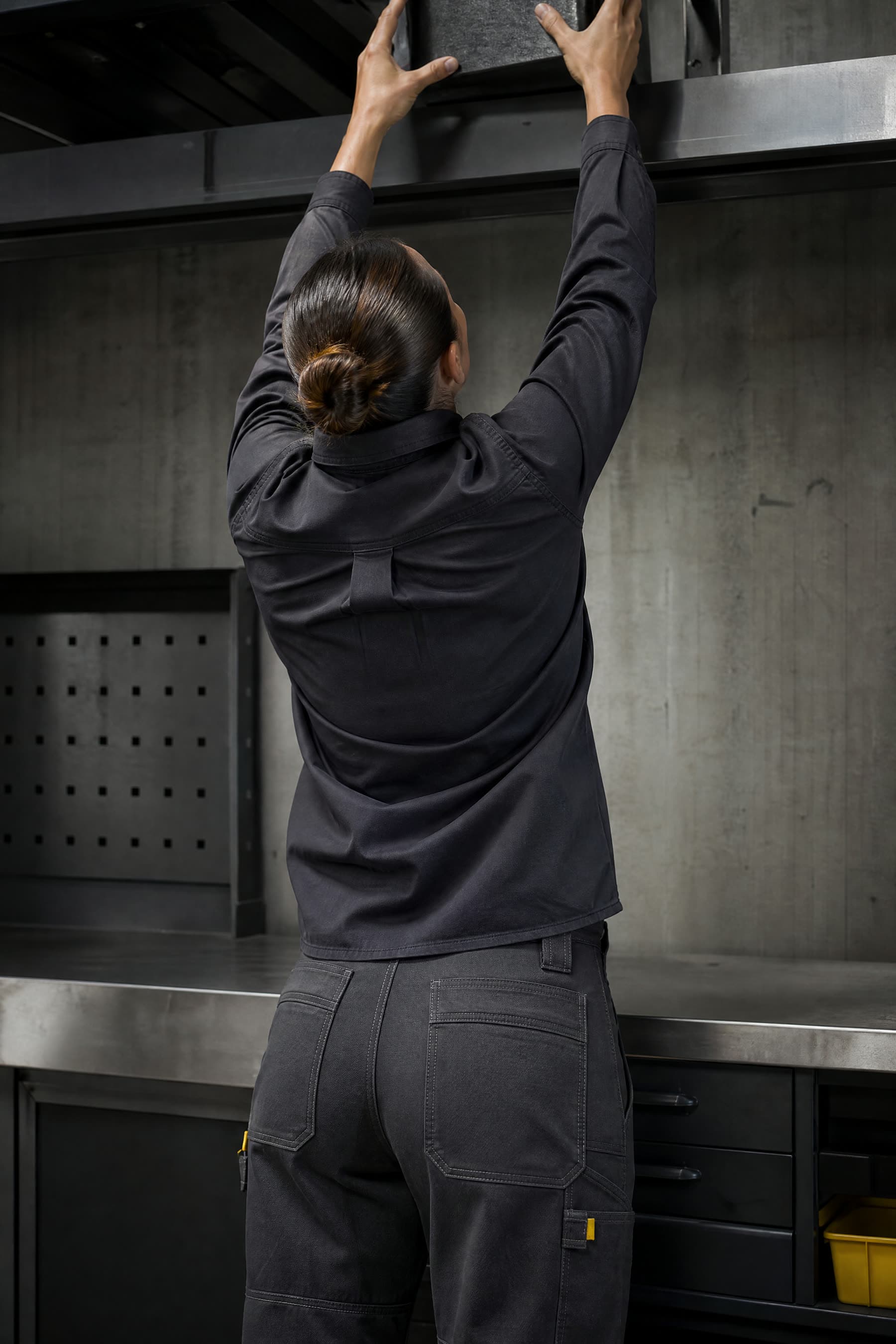 Rear view of both arms reaching overhead in a Truecut action-back work shirt, the hem staying at the waist.